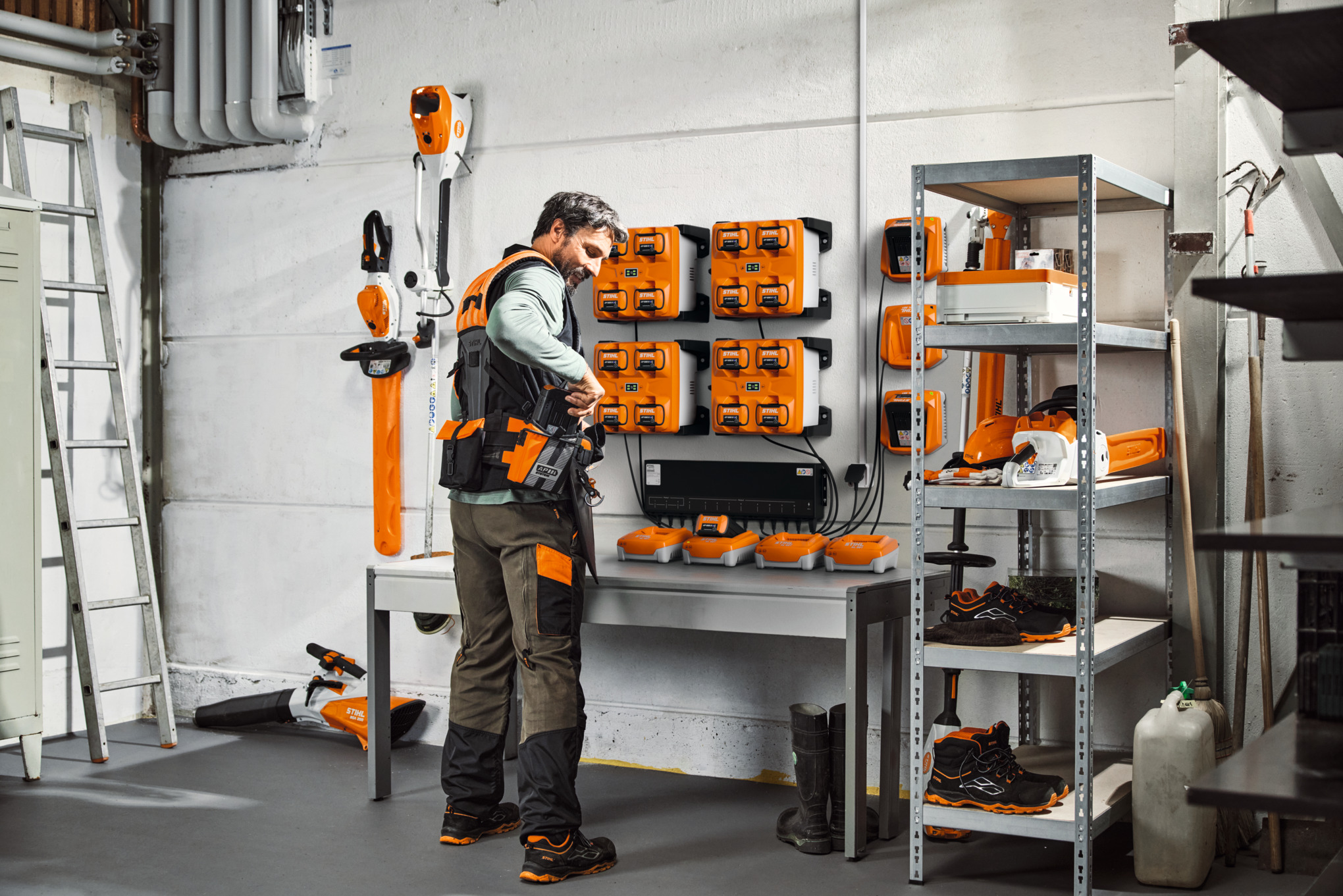 A man in a storage room with STIHL tools and batteries wears the STIHL ADVANCE X-Flex modular harness system.