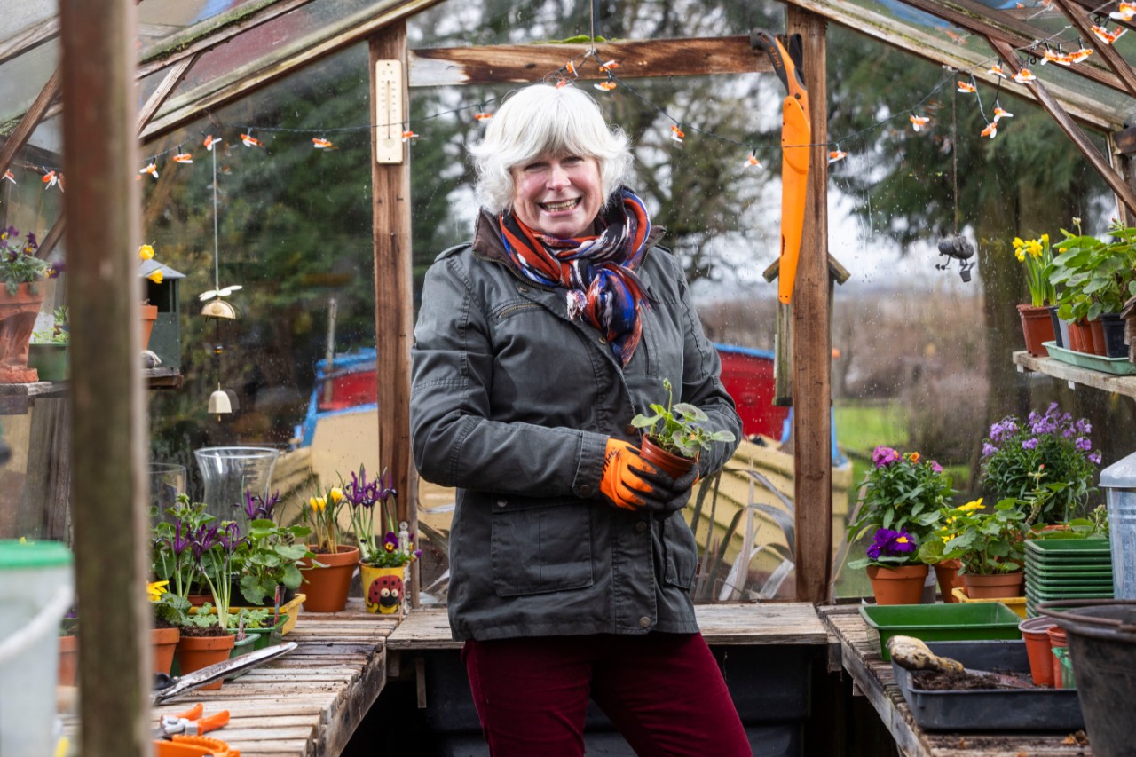 award-winning gardener Jane Moore holds potted plant in greenhouse