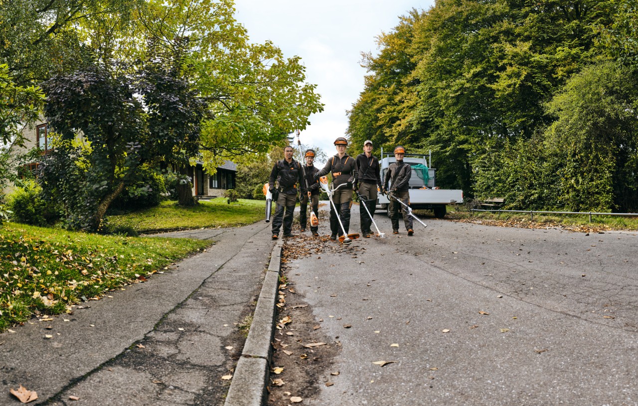 Five people in STIHL personal protective equipment walk next to each other on a path carrying various STIHL cordless power tools