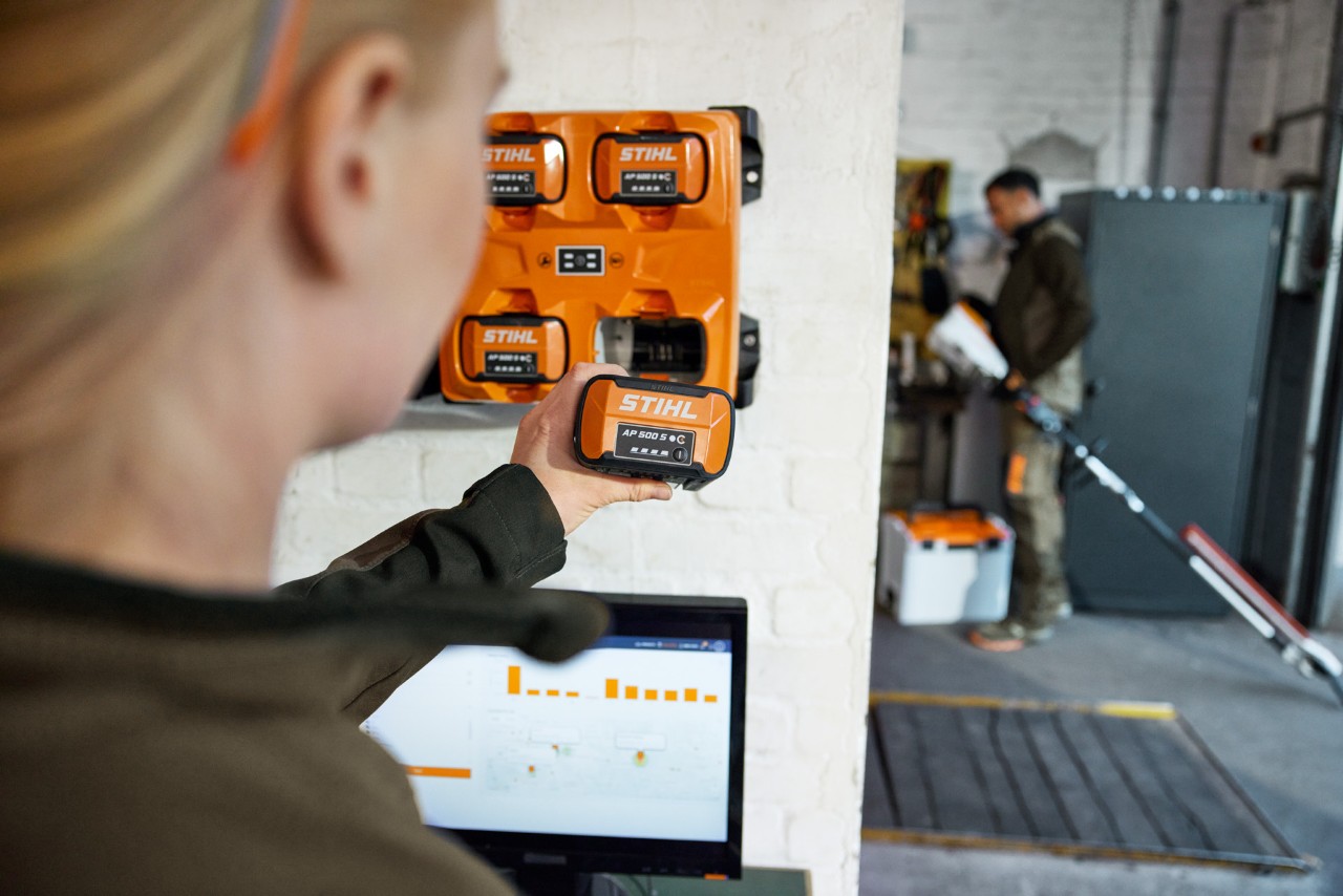 A woman in front of a laptop removing an AP 300 S from a STIHL AL 301-4 multi-charger