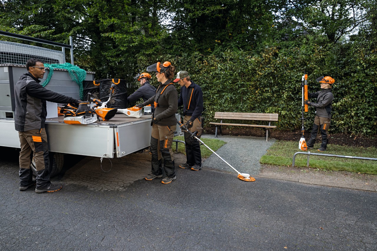 Gardeners and landscapers take STIHL AP-System power tools and a backpack battery from their vehicle’s loading area. 