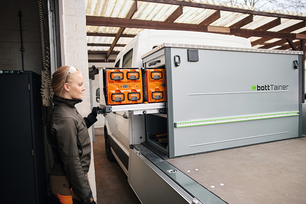 Side profile of a blonde woman next to a flatbed vehicle handling the batteries in the bottTainer.