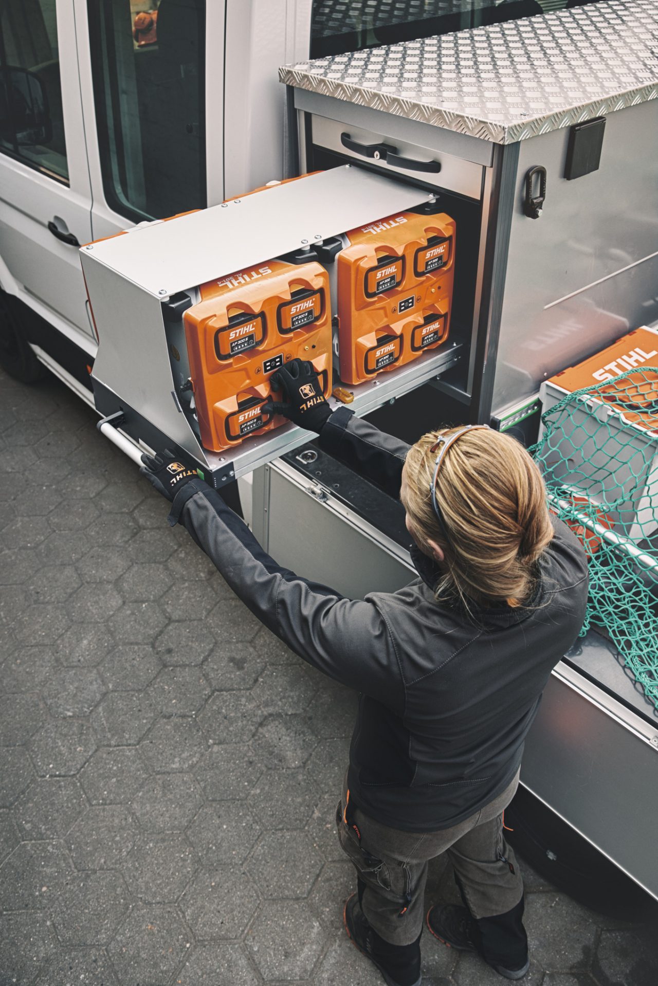 Overhead view of a blonde woman in STIHL work clothing next to a flatbed vehicle loading or unloading a bottTainer