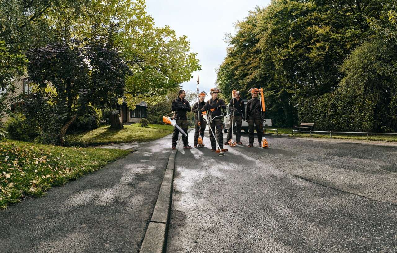 group of professional with garden power tools walking down tree-lined road