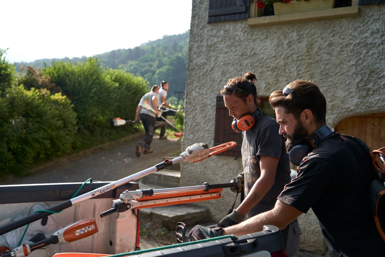Two landscape gardeners unloading STIHL battery-powered tools from a car, with other workers in the background 