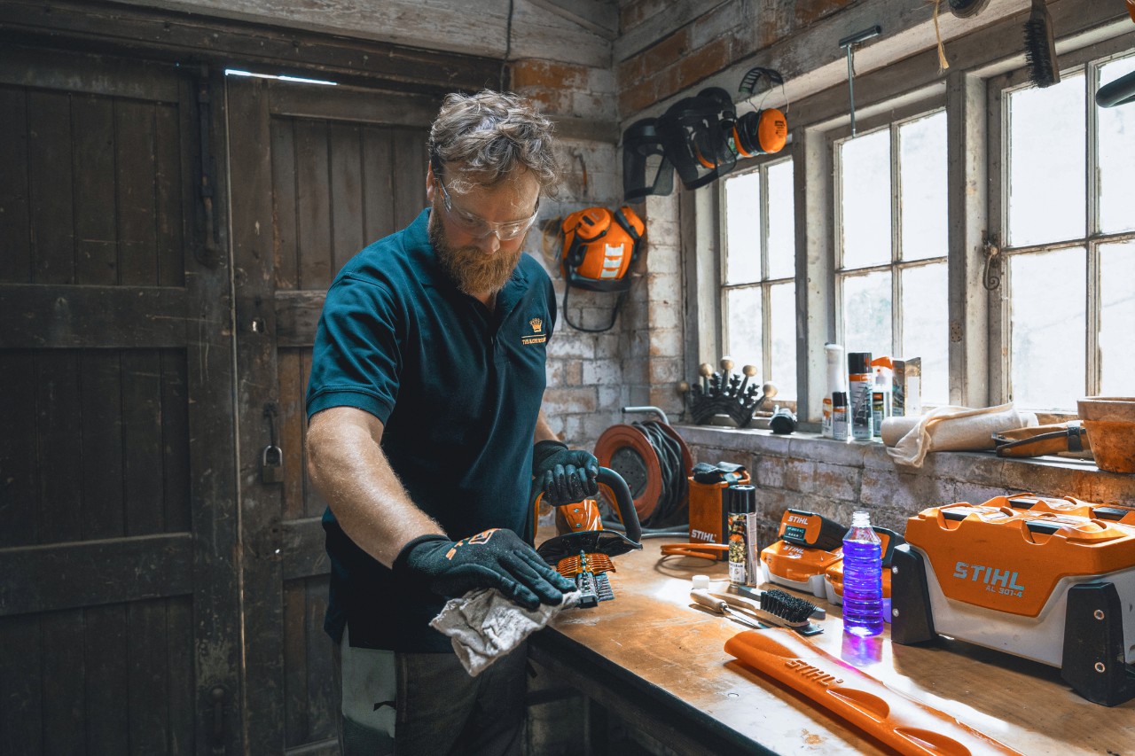 A man in a workshop wipes a STIHL hedge trimmer with a cloth