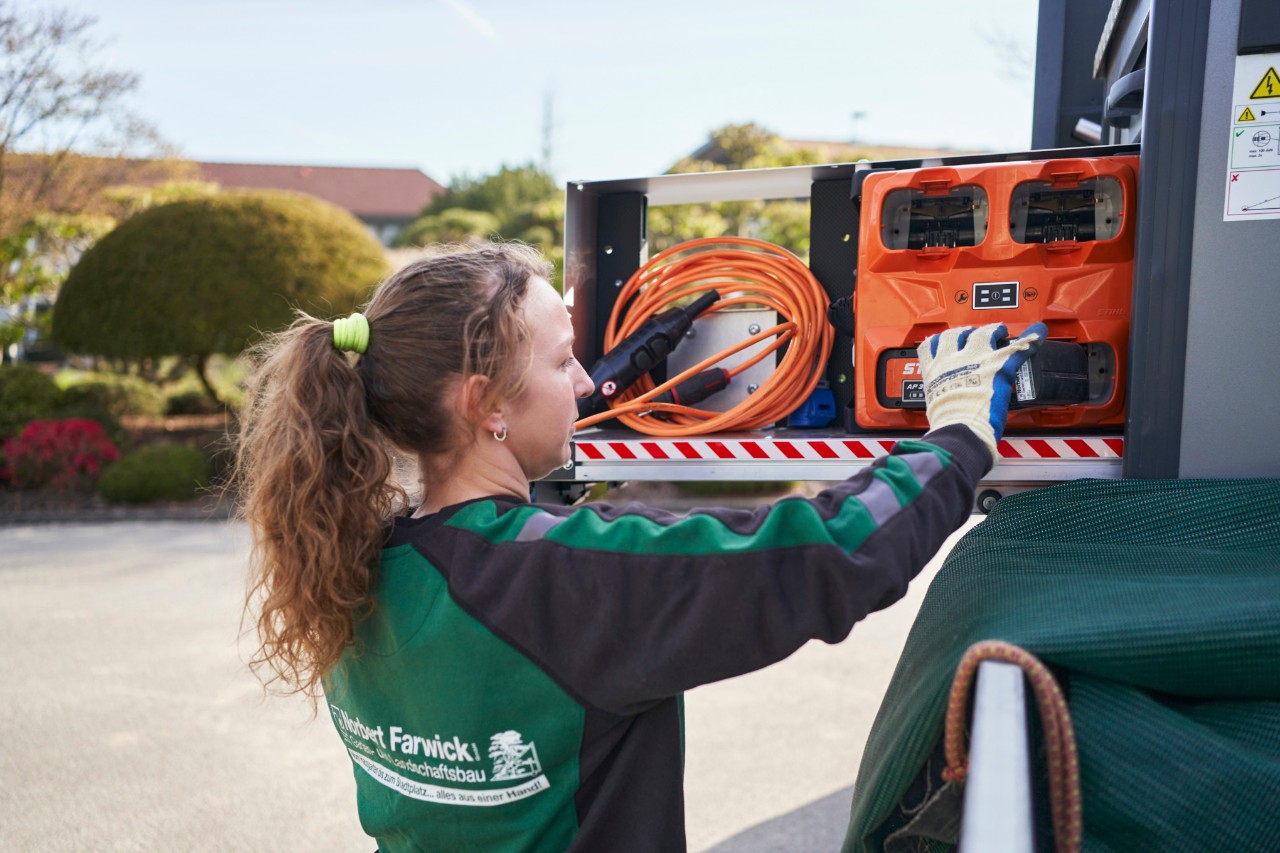 An employee of Farwick GmbH loads batteries into a bottTainer onto an emergency vehicle