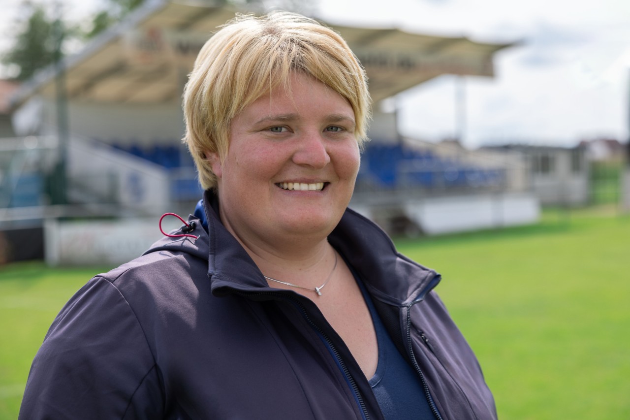 Greenkeeper Lesly Huber stands on the SC Sand sports field and smiles to the camera
