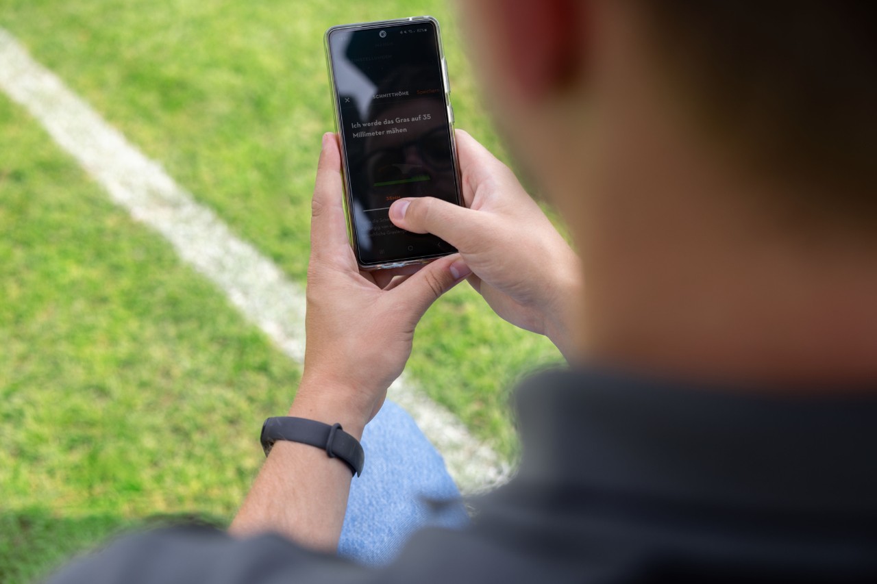 A person on a sports pitch with the MY iMOW® app open on a mobile phone