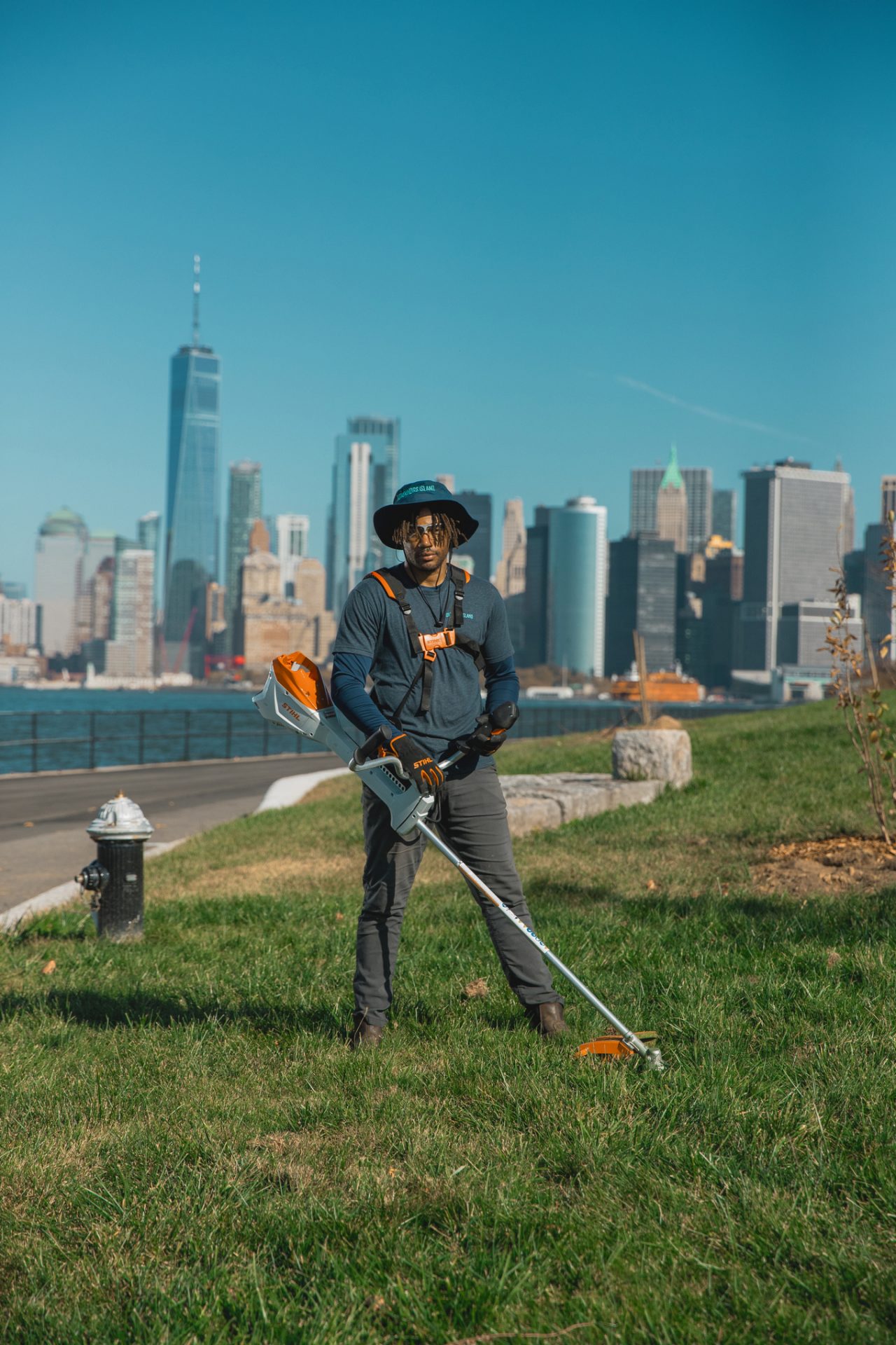 Governors Island employees wearing work gloves stand on the lawn holding an FSA 200 cordless motorized scythe