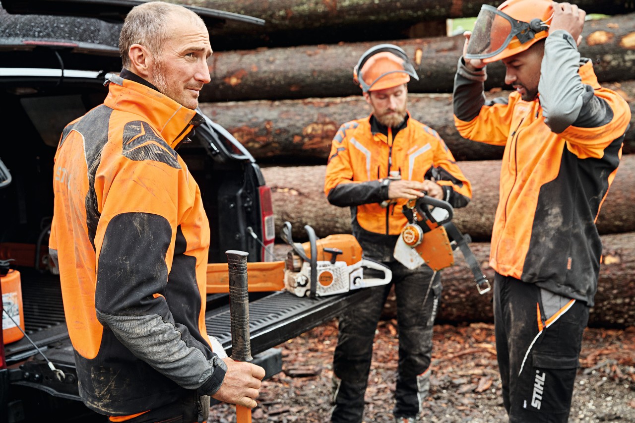 Three men in STIHL protective equipment and with STIHL cordless power tools in front of the loading area of a vehicle