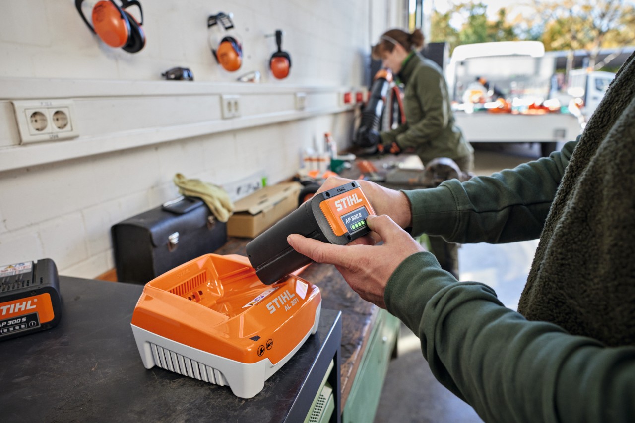 A person plugging a STIHL AP 300 S battery into a STIHL AL 301 high-speed charger