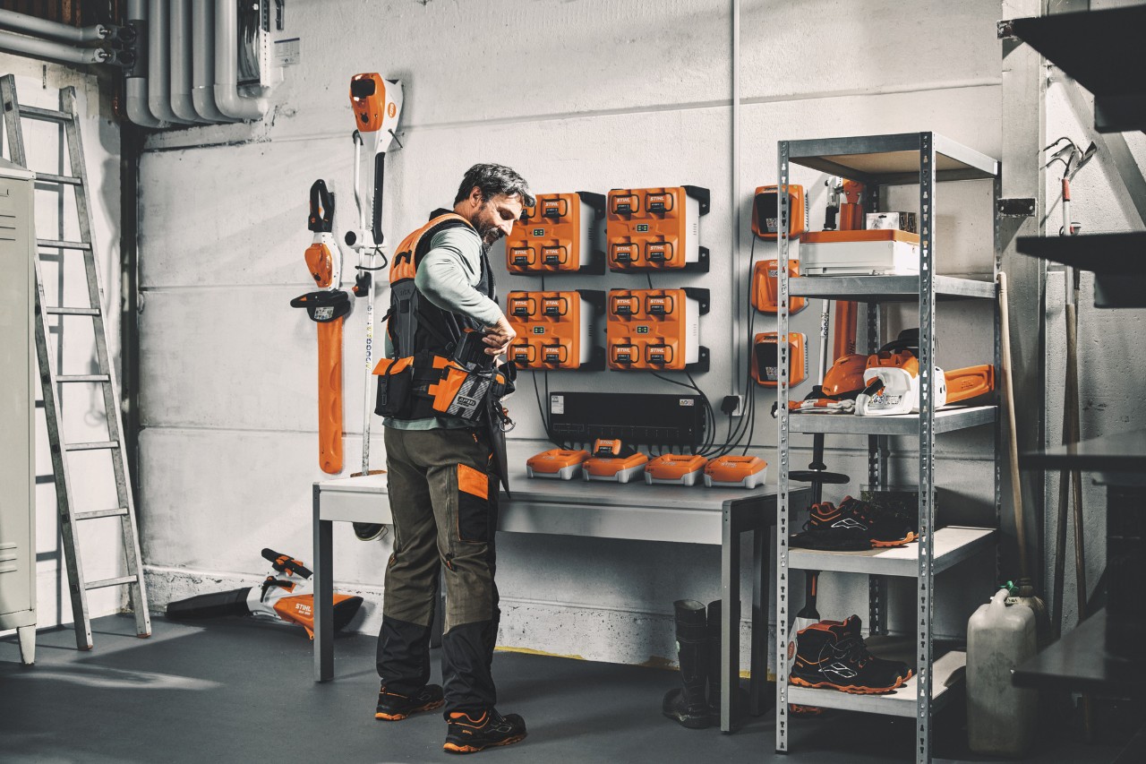 A man in a storage room with STIHL power tools and batteries wearing the STIHL ADVANCE X-Flex modular harness system 