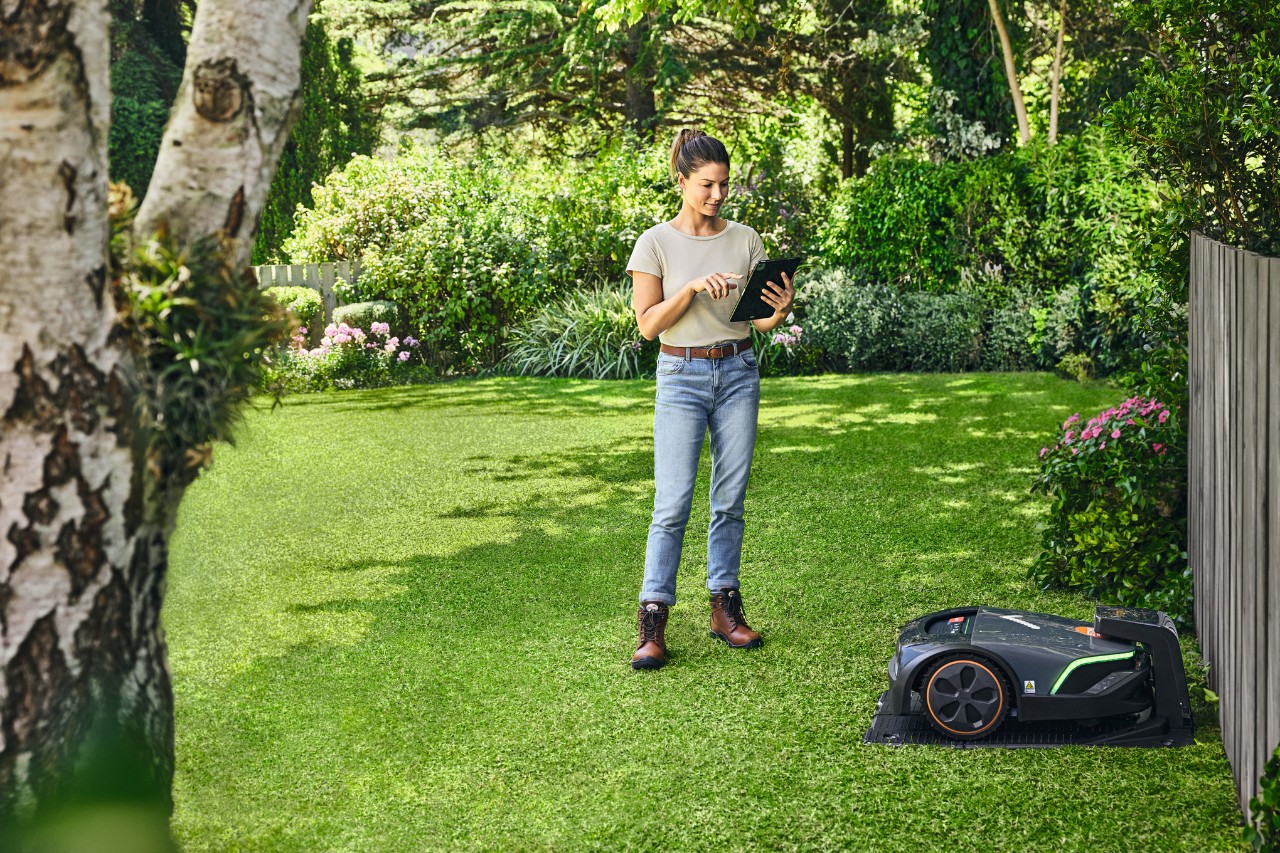 A woman operating the STIHL iMOW® EVO in her garden using a tablet
