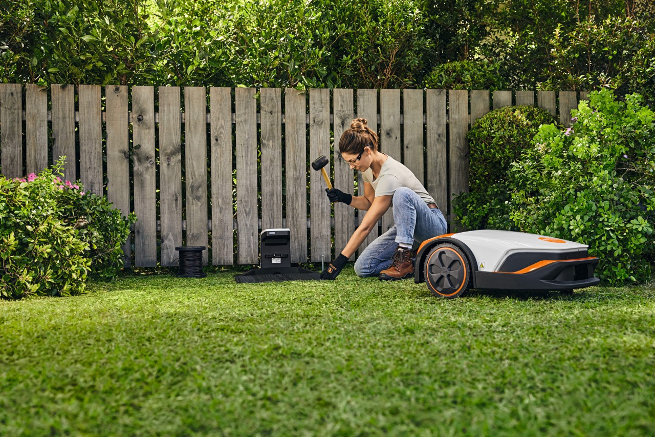 A woman installing the docking station for her STIHL iMOW® in front of a fence in her garden.