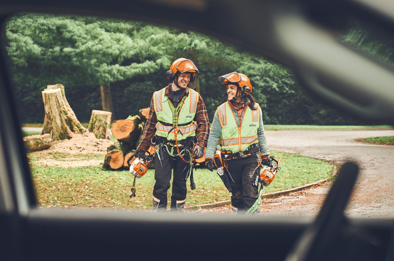 A man and a woman with STIHL cordless chainsaws and a STIHL cordless pruner walk smiling towards a car  
